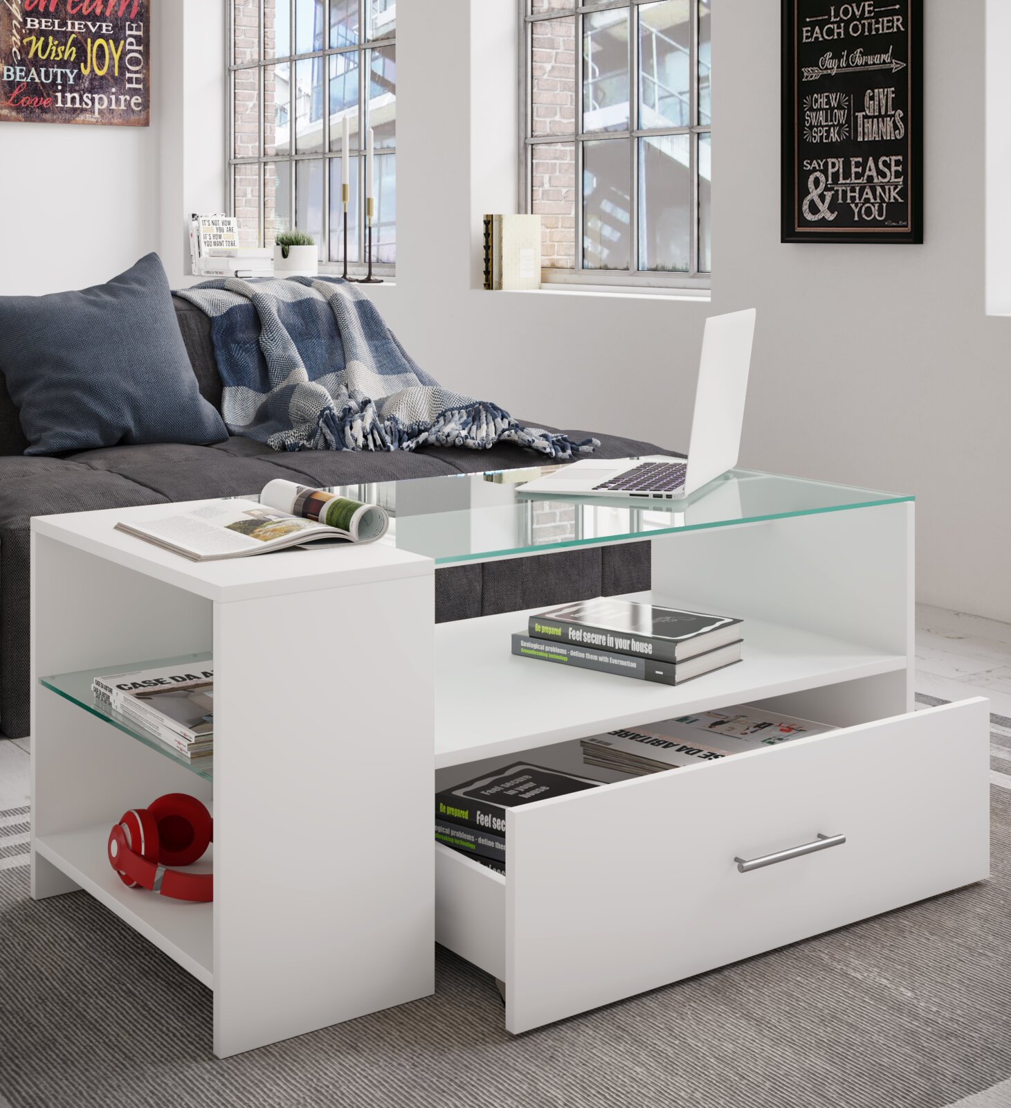 Moderner weißer Couchtisch mit Glasplatte, offener Ablage und Schublade, beladen mit Büchern und Laptop, in Wohnzimmer vor grauem Sofa – Perspektive: frontale leicht schräge Ansicht von oben
