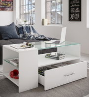 Moderner weißer Couchtisch mit Glasplatte, offener Ablage und Schublade, beladen mit Büchern und Laptop, in Wohnzimmer vor grauem Sofa – Perspektive: frontale leicht schräge Ansicht von oben