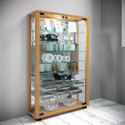 Hohe Glasvitrine mit hellem Holzrahmen, Glastüren und mehreren Glasböden, dekorativ bestückt; Ansicht schräg von vorne (leicht von links)
