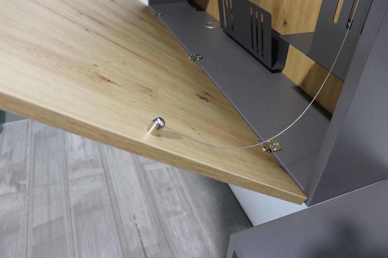 Nahaufnahme eines Wandschreibtischs mit heruntergeklappter Holzplatte und Metallhalterungen, seitliche Perspektive.