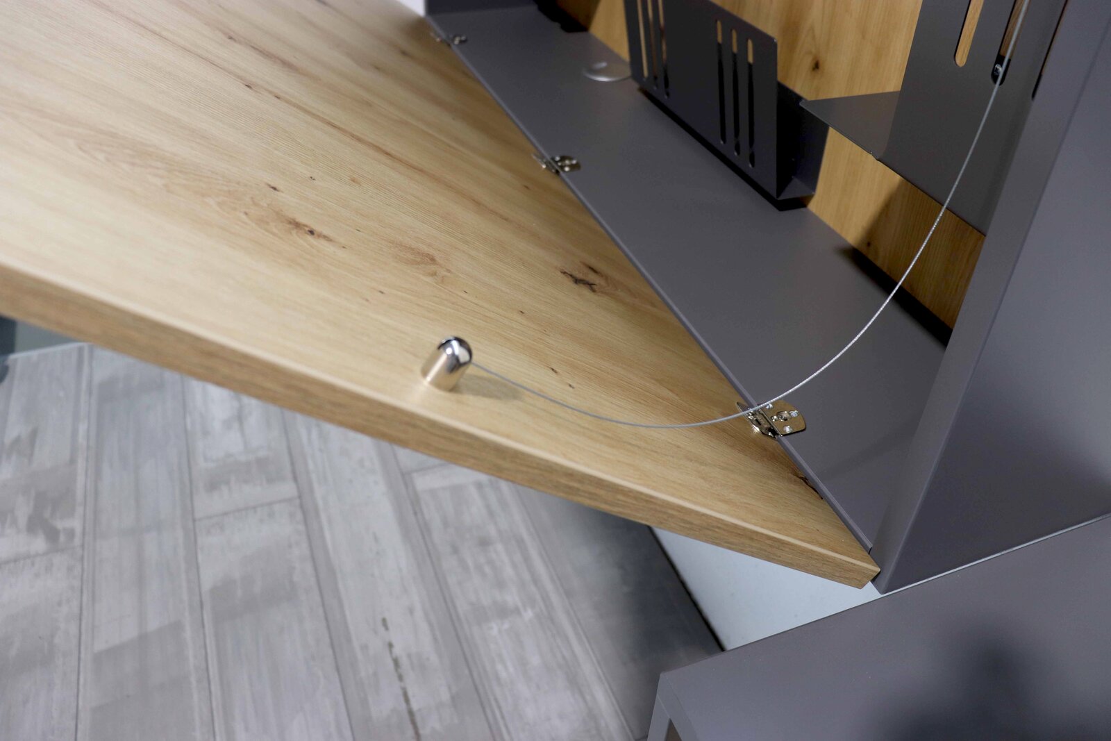 Nahaufnahme eines Wandschreibtischs mit heruntergeklappter Holzplatte und Metallhalterungen, seitliche Perspektive.