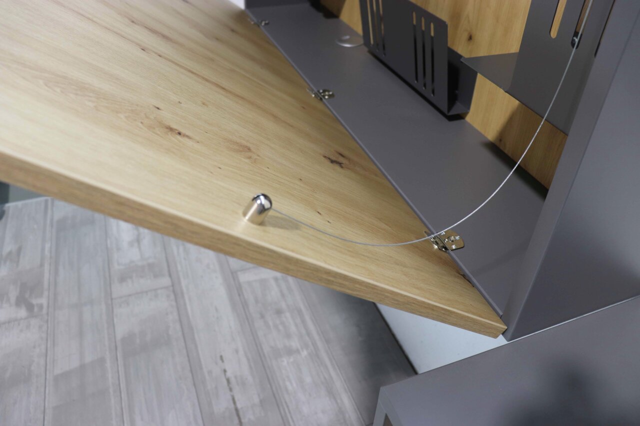 Close-up van een wandbureau met neergelaten houten blad en metalen beugels, gezien vanaf de zijkant.