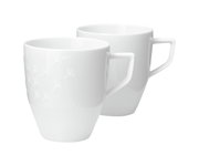 Zwei weiße Becher mit Henkel, einer mit dezentem Muster, aus seitlicher Perspektive fotografiert.