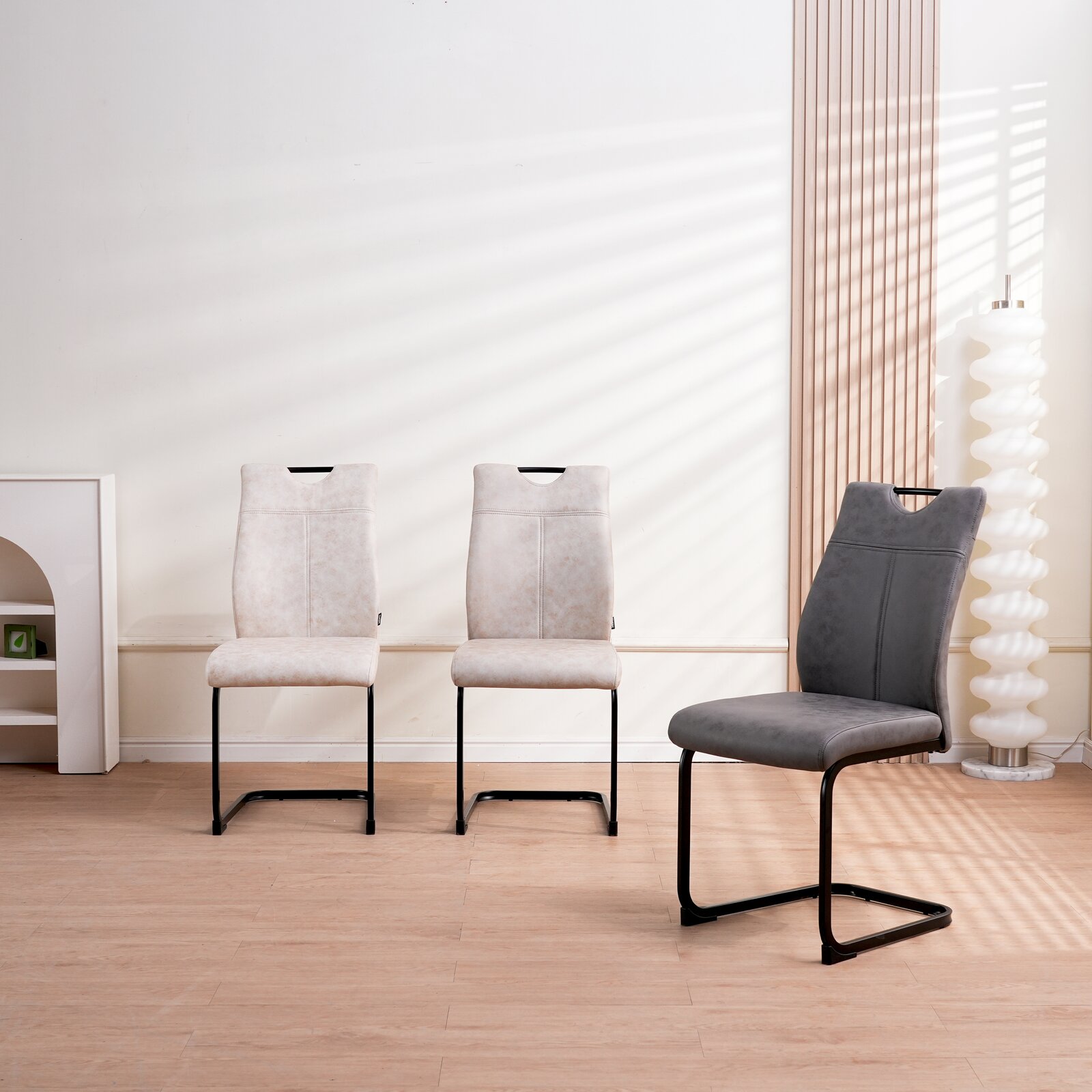 Drei Schwingstühle in einem modernen Raum, zwei in hellem Beige und einer in Dunkelgrau, seitliche Perspektive.