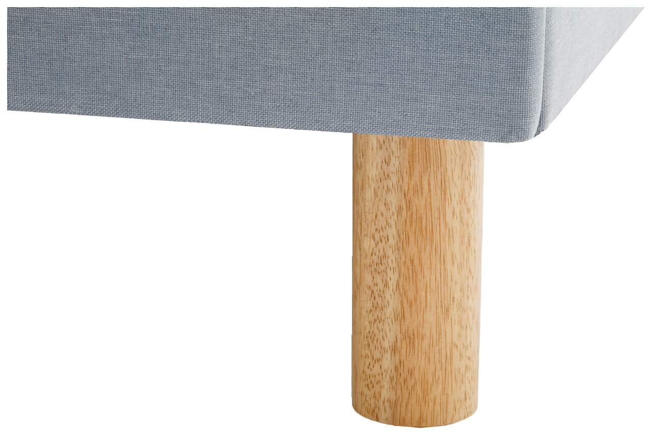 Close-up van een gestoffeerd bed met een lichtgrijze stoffen bekleding en een ronde houten voet, gezien vanaf de zijkant.