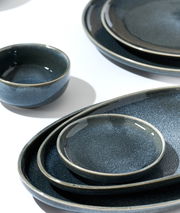 Verschiedene dunkelblaue Keramikteller und Schalen in einer Nahaufnahme, von oben betrachtet, auf einem weißen Hintergrund arrangiert.