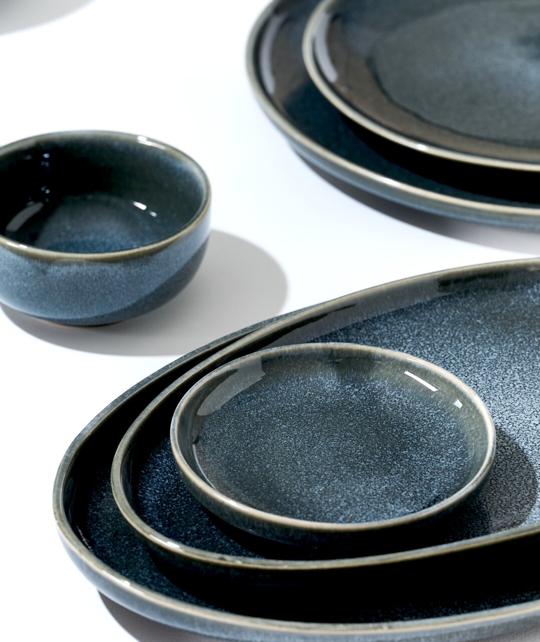 Verschiedene dunkelblaue Keramikteller und Schalen in einer Nahaufnahme, von oben betrachtet, auf einem weißen Hintergrund arrangiert.