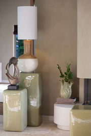 Elegante Vase mit wellenförmigem Design, aus grünlicher Keramik, auf einem Tisch neben dekorativen Elementen, seitliche Perspektive.