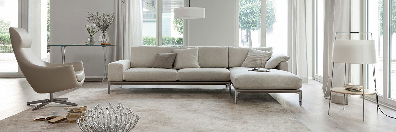 Ein modernes, schlichtes Wohnzimmer mit einem hellen Sofa einem Ohrensessel der Bielefelder Werkstätten