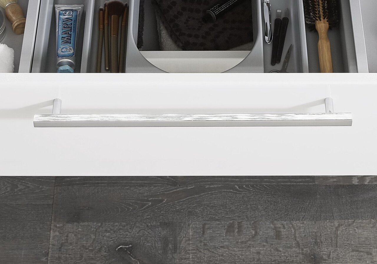 Nahaufnahme einer geöffneten Schublade mit verschiedenen Pflegeprodukten und Accessoires, darunter Zahnpasta, Pinsel und Bürste, in einem modernen Badezimmer.