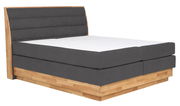 Boxspringbett mit grauem Polster und Holzrahmen, seitliche Perspektive