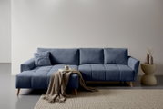Blaues, modern gepolstertes Ecksofa mit linksseitiger Ottomane, gesteppten Sitzflächen und Holzfüßen, frontal in leichter Schrägansicht fotografiert; davor Decke und Bücher, daneben Beistelltisch mit Vasen.