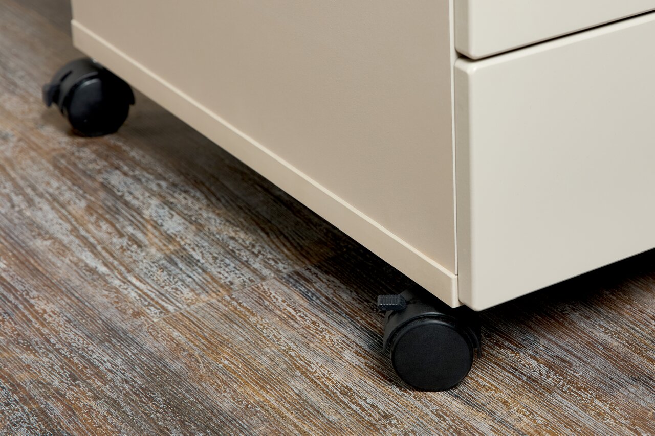 Nahaufnahme eines Rollcontainers mit schwarzen Rollen auf einem Holzboden, seitliche Perspektive