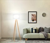 Moderne Stehleuchte mit dreibeinigem Holzgestell und weißem Lampenschirm, seitliche Perspektive im Wohnzimmer.