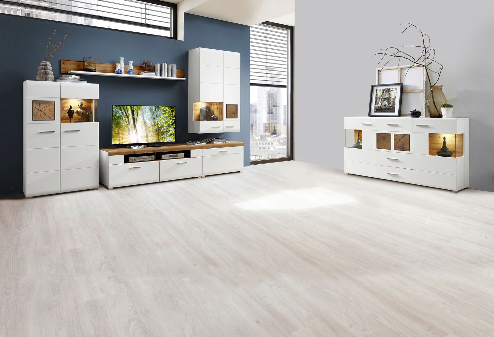 Moderne Wohnwand und Sideboard in Weiß mit Holzakzenten, frontal fotografiert in einem hellen Raum mit großen Fenstern.