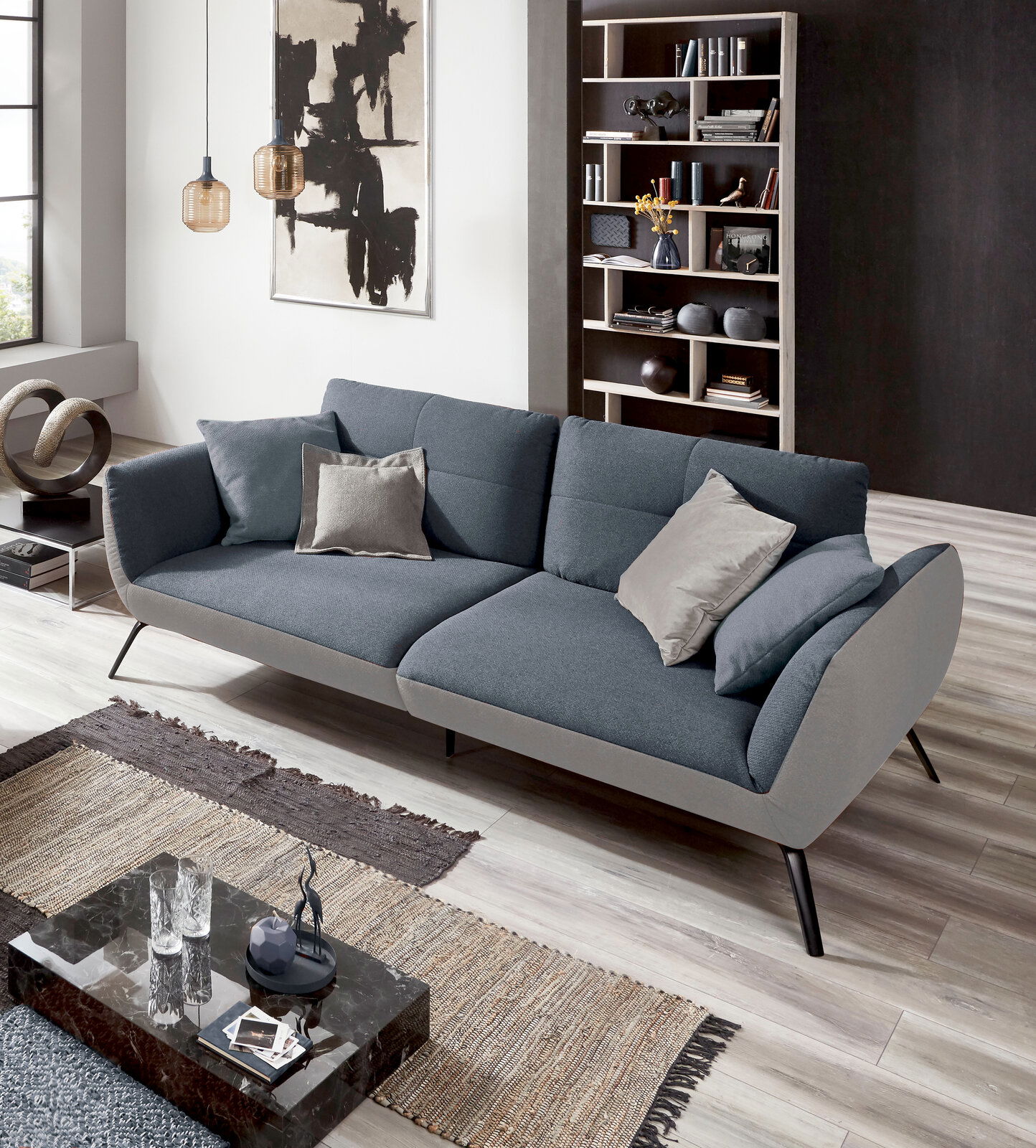 StepOne Sofa NEWPORT Modernes Sofa in Grau mit Kissen, seitliche Perspektive, in stilvollem Wohnzimmer mit Kunstwerk und Bücherregal.