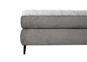 Seitliche Nahaufnahme eines grauen Boxspringbetts mit gestepptem Kopfteil und schwarzen Beinen.