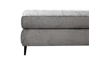 Seitliche Nahaufnahme eines grauen Boxspringbetts mit gestepptem Kopfteil und schwarzen Beinen.