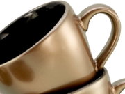 Nahaufnahme einer metallic-goldenen Kaffeetasse mit Henkel und schwarzer Innenlasur, schräg von oben seitlich fotografiert vor weißem Hintergrund.