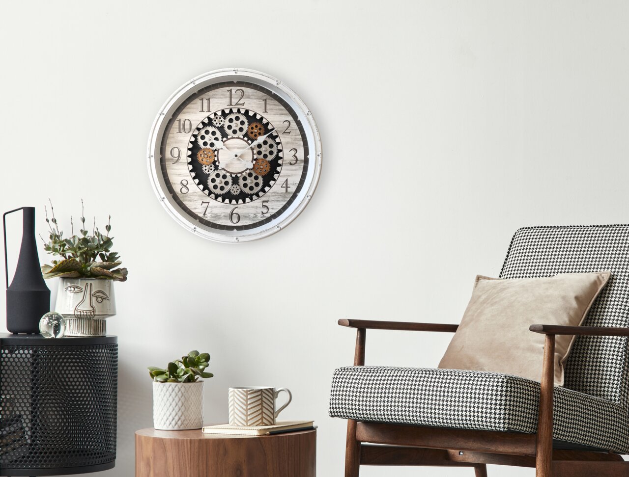 Wanduhr mit Zahnrädern im Vintage-Stil an einer weißen Wand, umgeben von moderner Dekoration und einem Sessel, aus frontaler Perspektive.