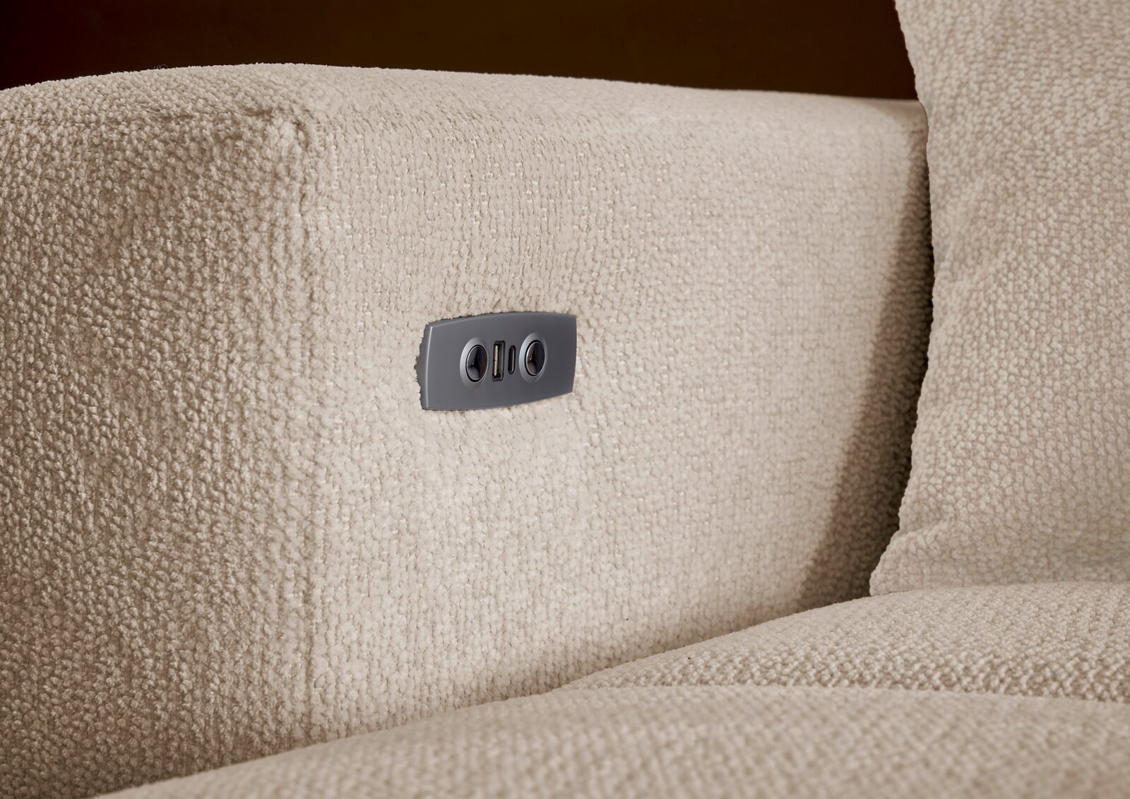 Nahaufnahme der seitlichen Armlehne eines beigen Bouclé-Sofas mit integrierter USB-Ladebuchse in Metallblende, perspektivisch leicht von vorne und seitlich aufgenommen