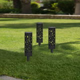 Drei schwarze Solarleuchten mit dekorativem Muster, aufrecht im grünen Rasen stehend, aus seitlicher Perspektive fotografiert.