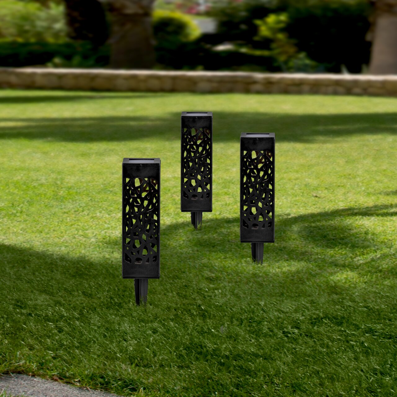Drei schwarze Solarleuchten mit dekorativem Muster, aufrecht im grünen Rasen stehend, aus seitlicher Perspektive fotografiert.