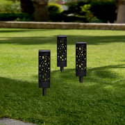 Drei schwarze Solarleuchten mit dekorativem Muster, aufrecht im grünen Rasen stehend, aus seitlicher Perspektive fotografiert.