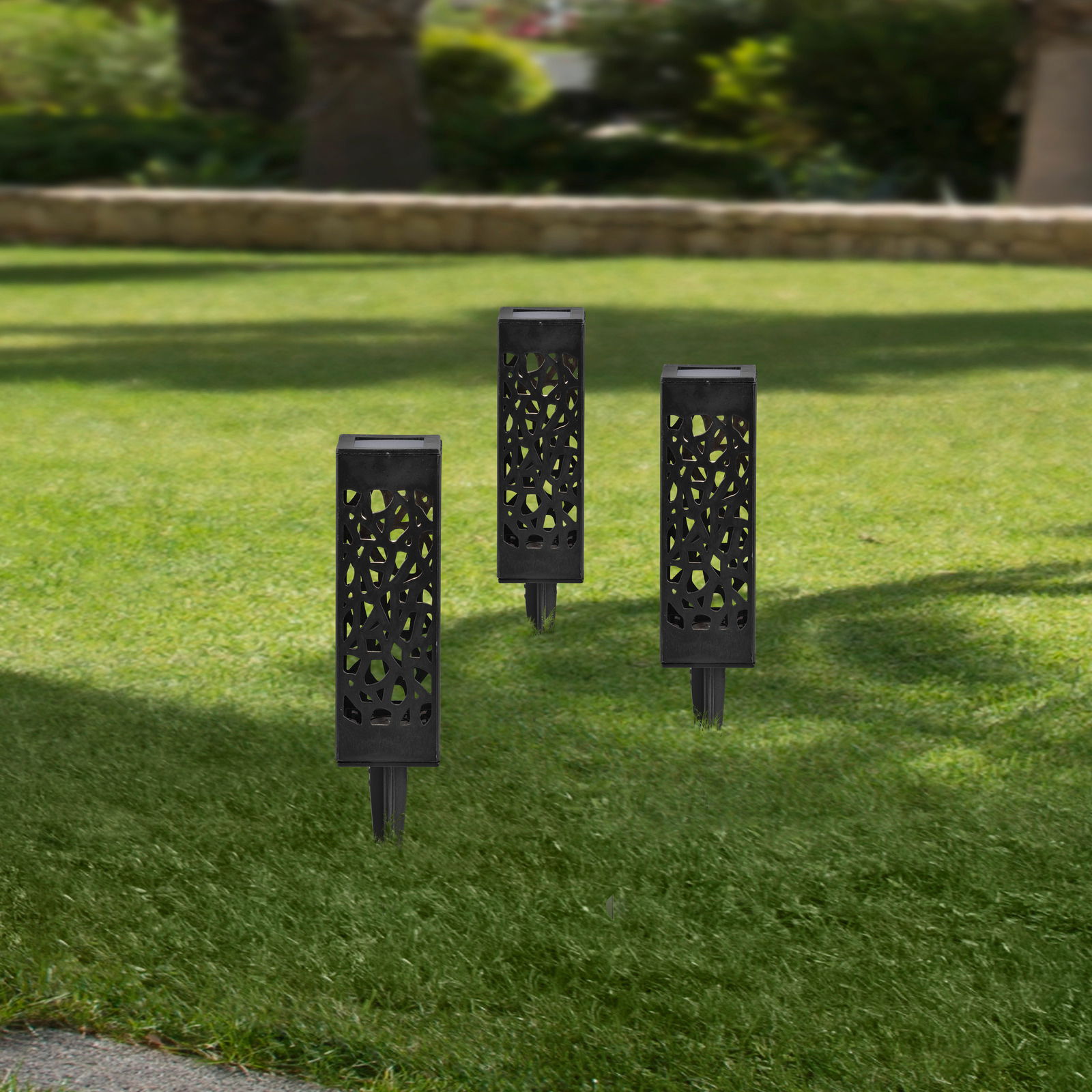 Drei schwarze Solarleuchten mit dekorativem Muster, aufrecht im grünen Rasen stehend, aus seitlicher Perspektive fotografiert.