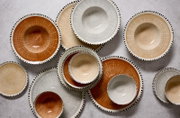 Bovenaanzicht van een decoratief servies met kommen en borden in warme aardetinten en grijs, voorzien van een verfijnd lijnpatroon en een zwart gestippelde rand.