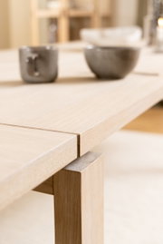 Nahaufnahme einer hellen Holztischplatte mit Ansteckplatte, im Hintergrund unscharf zwei graue Tassen. Perspektive von der Seite.