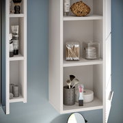 Nahaufnahme eines weißen Badezimmerschranks mit offenen Regalen, gefüllt mit Pflegeprodukten und Accessoires, aus einer seitlichen Perspektive.