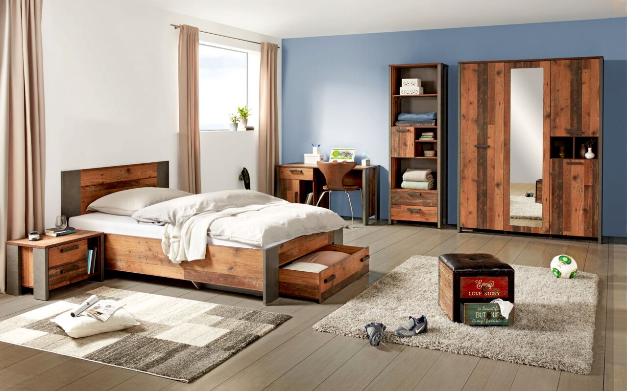 Slaapkamermeubelset in moderne houtlook, bestaande uit een bed met opberglade, een nachtkastje, een plank, een bureau en een drievleugelige draaikast met spiegel. Perspectief: vooraanzicht van de volledige set in een lichte kamer met blauwe muren.