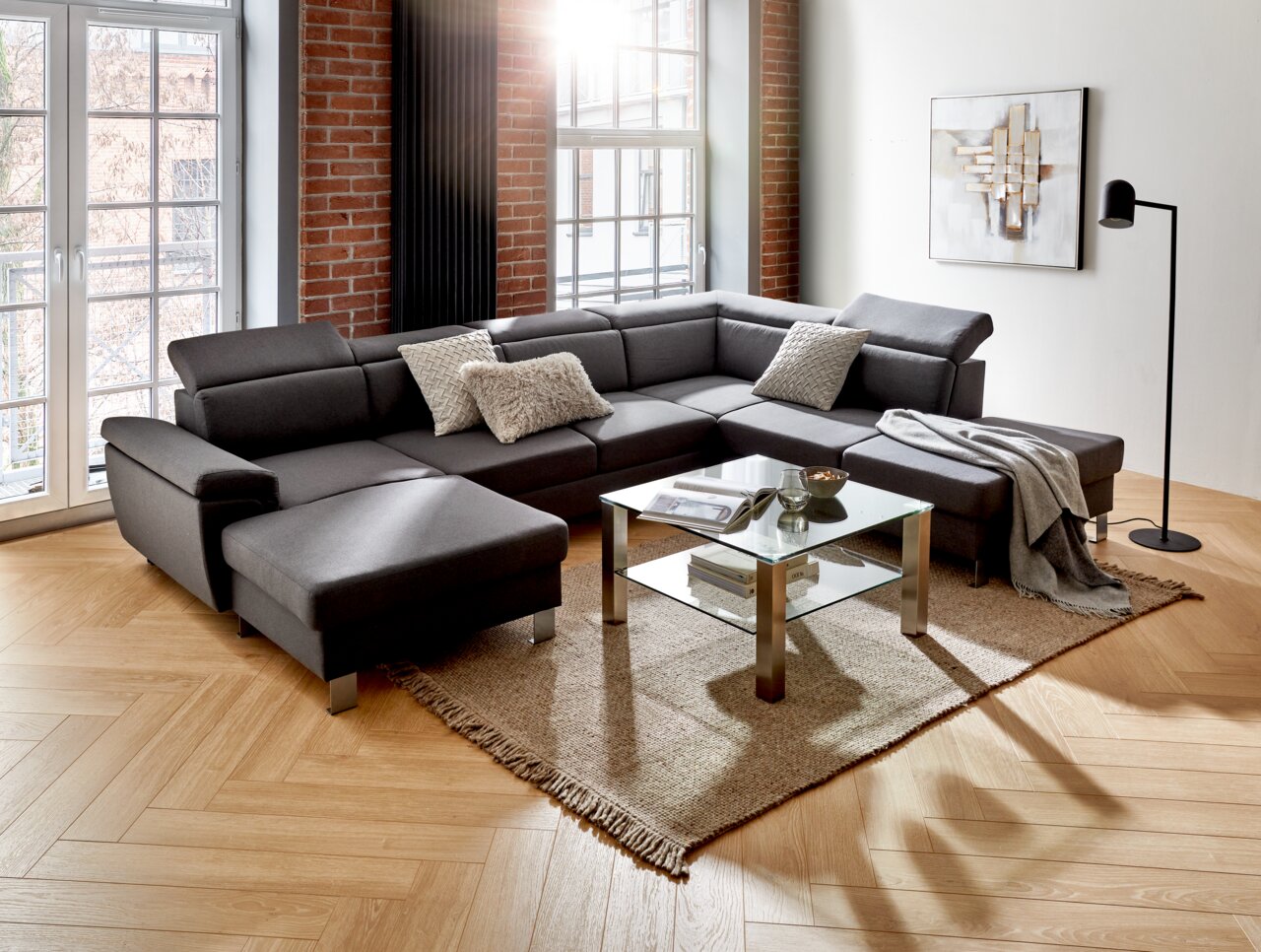 Moderne graue Rundecke in einem stilvollen Wohnzimmer mit großen Fenstern, Holzboden und dekorativen Kissen, aus der Perspektive von vorne links.