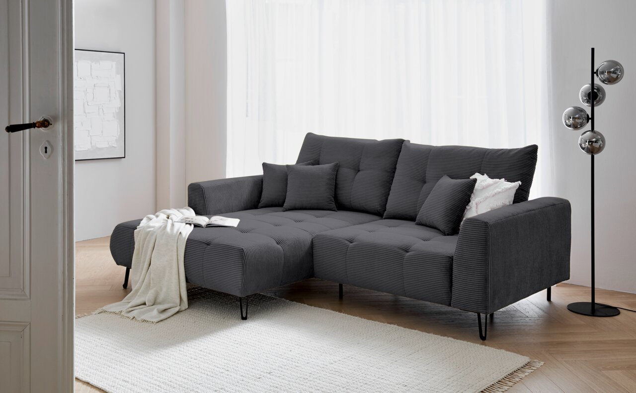 Z2 Hoekbank SWING Grijze hoekbank met poef aan de linkerkant, versierd met kussens en een deken, in een moderne woonkamer met een lichte houten vloer en een staande lamp, gezien van voren.