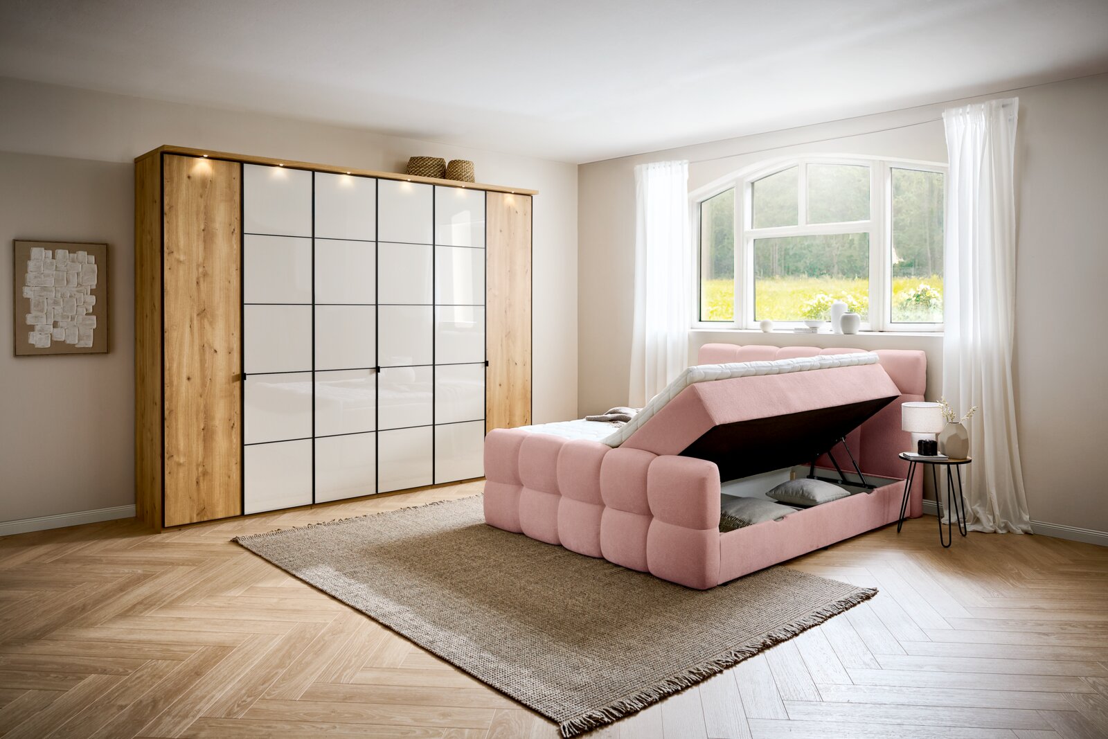 Boxbett in einem modernen Schlafzimmer, seitliche Perspektive, mit Stauraum unter der Matratze, rosa Polsterung und hellem Holzboden.