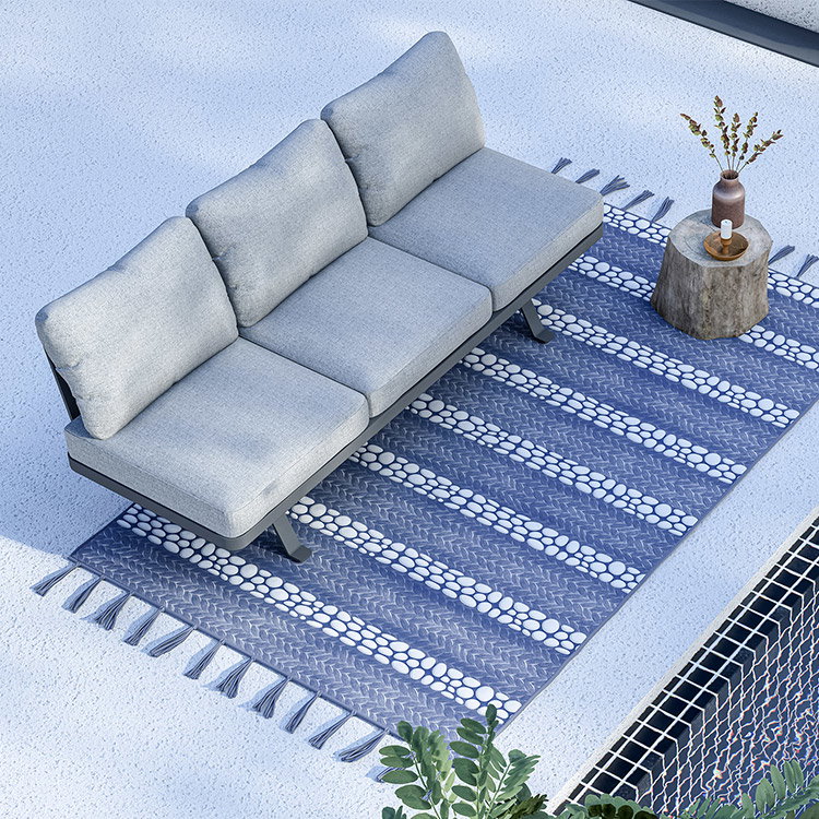 Graues Outdoor-Sofa auf gemustertem Teppich mit Beistelltisch und Dekovase im Freien.