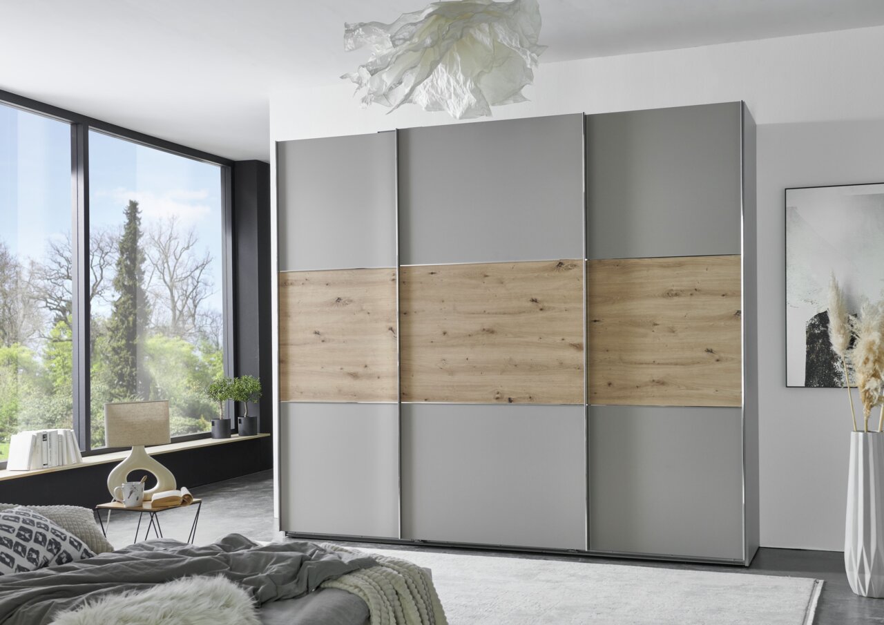 Moderner dreitüriger Schwebetürenschrank in Grau mit Holzelementen, frontal im Schlafzimmer platziert.