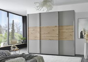 Moderner dreitüriger Schwebetürenschrank in Grau mit Holzelementen, frontal im Schlafzimmer platziert.