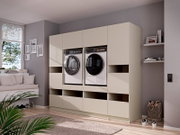 Modernes, cremefarbenes Einbauschrank-System für Waschküche mit integrierter Waschmaschine und Trockner in einem hellen Wohnraum, frontal in leichter Schrägansicht von links aufgenommen