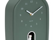 Grüne Wanduhr mit weißen Ziffern und Zeigern, zeigt die Zeit 2:10 an, mit einer kleinen weißen Katze in einer Öffnung unten. Perspektive von schräg vorne.