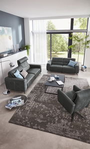 Modernes Wohnzimmer mit zwei grauen Sofas und einem Sessel, Blick von oben. Große Fenster mit Blick ins Grüne, stilvolle Dekoration und ein eleganter Teppich.