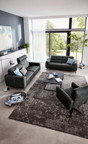 Modernes Wohnzimmer mit zwei grauen Sofas und einem Sessel, Blick von oben. Große Fenster mit Blick ins Grüne, stilvolle Dekoration und ein eleganter Teppich.