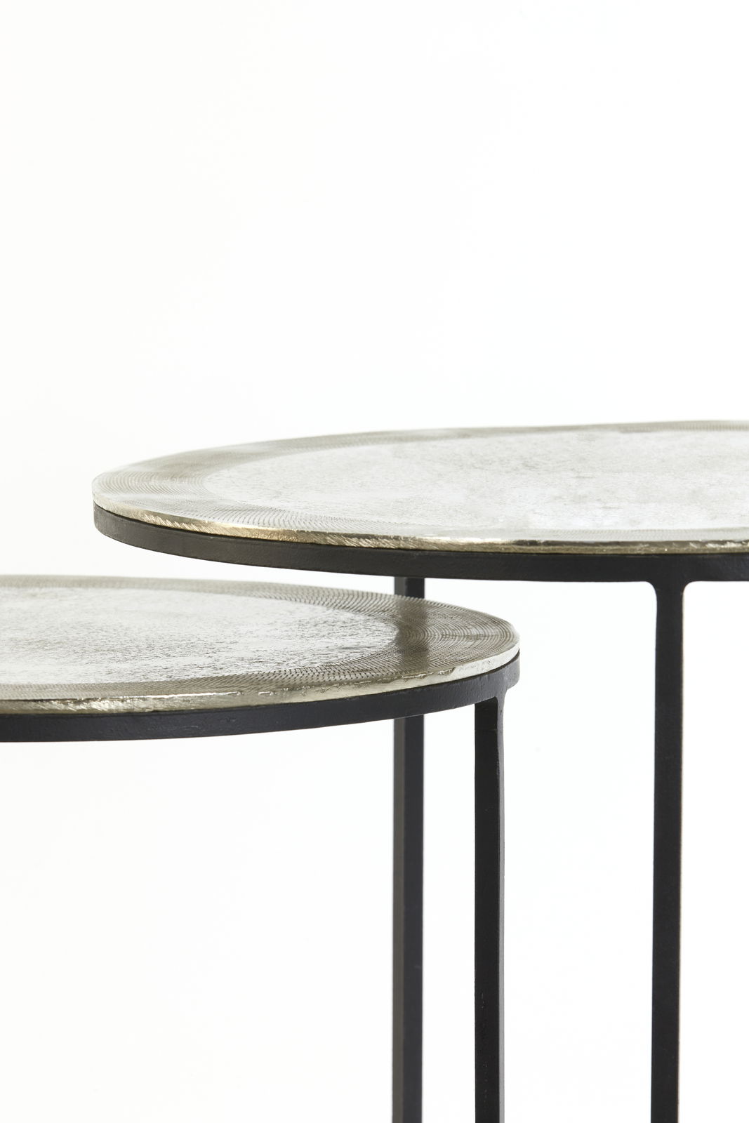 Nahaufnahme von zwei runden Beistelltischen mit Metalloberfläche und schlanken schwarzen Beinen, seitliche Perspektive.