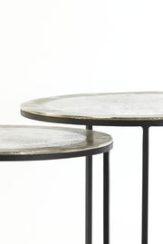 Nahaufnahme von zwei runden Beistelltischen mit Metalloberfläche und schlanken schwarzen Beinen, seitliche Perspektive.