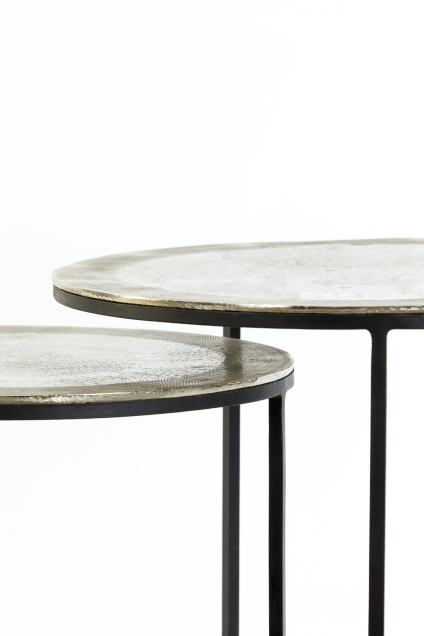 Nahaufnahme von zwei runden Beistelltischen mit Metalloberfläche und schlanken schwarzen Beinen, seitliche Perspektive.