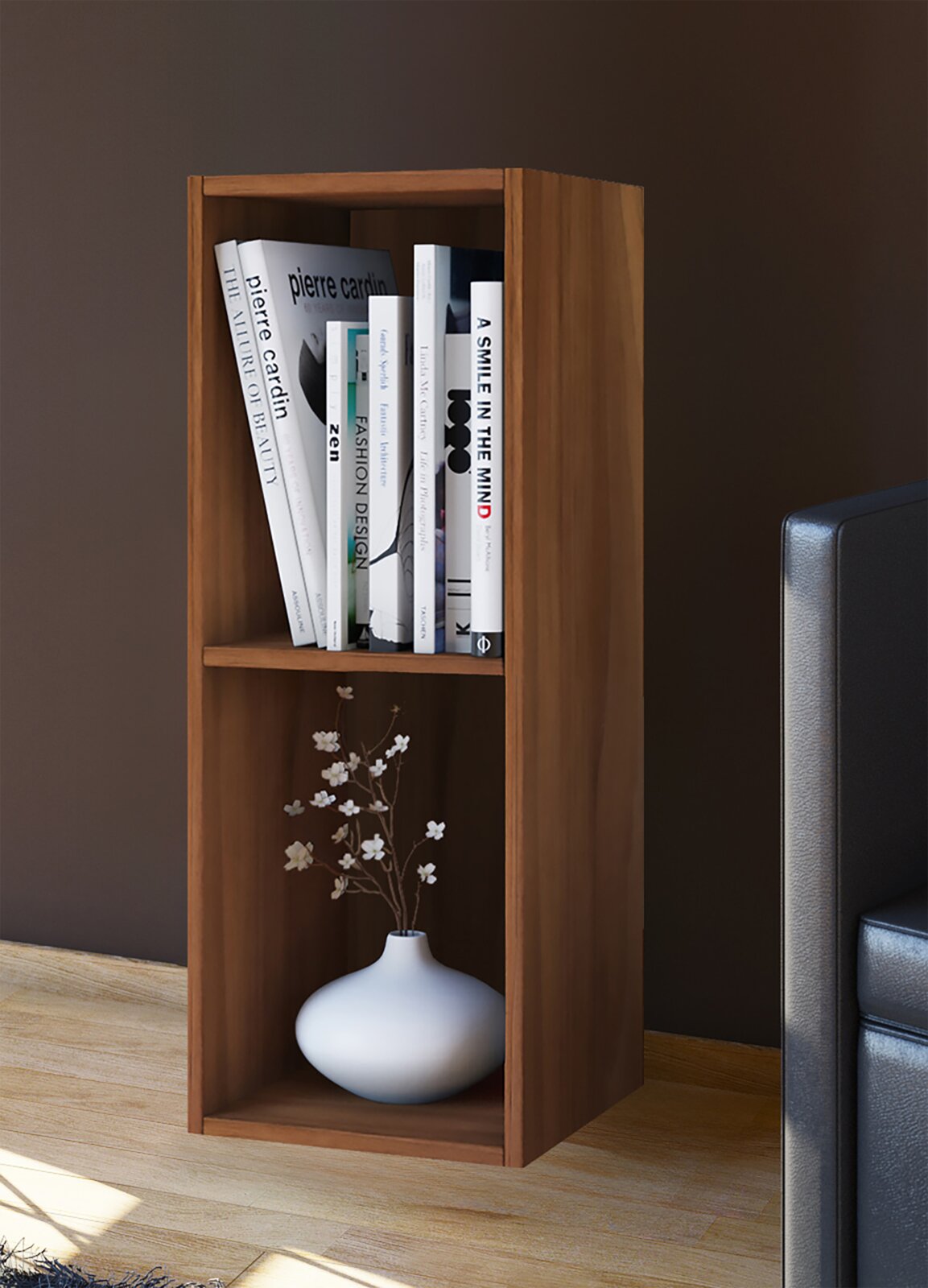 Schmales, zweifächriges Holzregal in warmem Braun neben einem Sofa, oben mit Büchern und unten mit weißer Vase und Zweigen dekoriert, aus frontaler leicht seitlicher Perspektive.