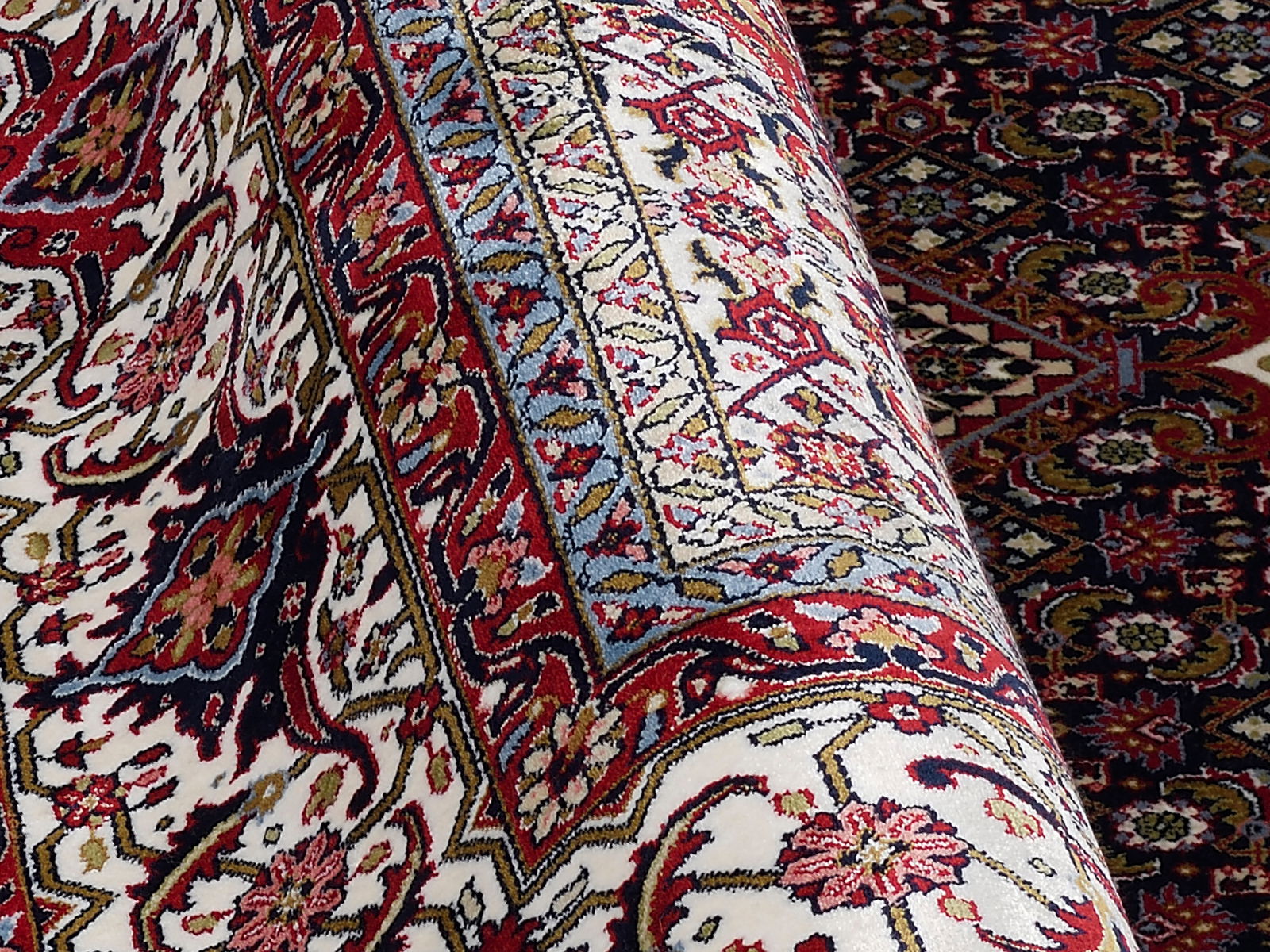 Nahaufnahme eines Orientteppichs mit detailliertem floralen Muster in Rot-, Blau- und Beigetönen, perspektivisch von der Seite aufgenommen.