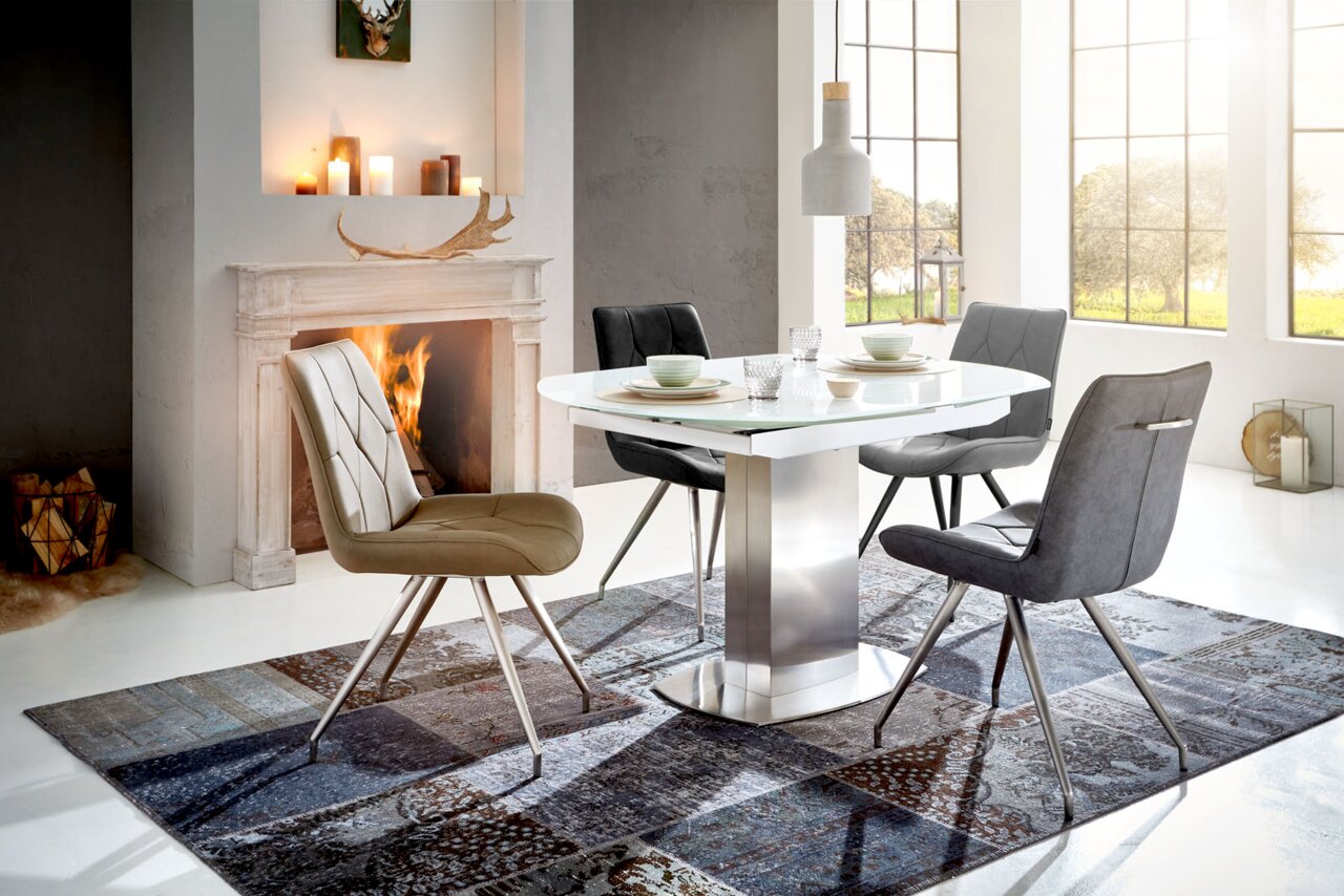 Moderner Essbereich mit einem eleganten Esstisch und vier stilvollen Stühlen, im Hintergrund ein Kamin und große Fenster, seitliche Perspektive.