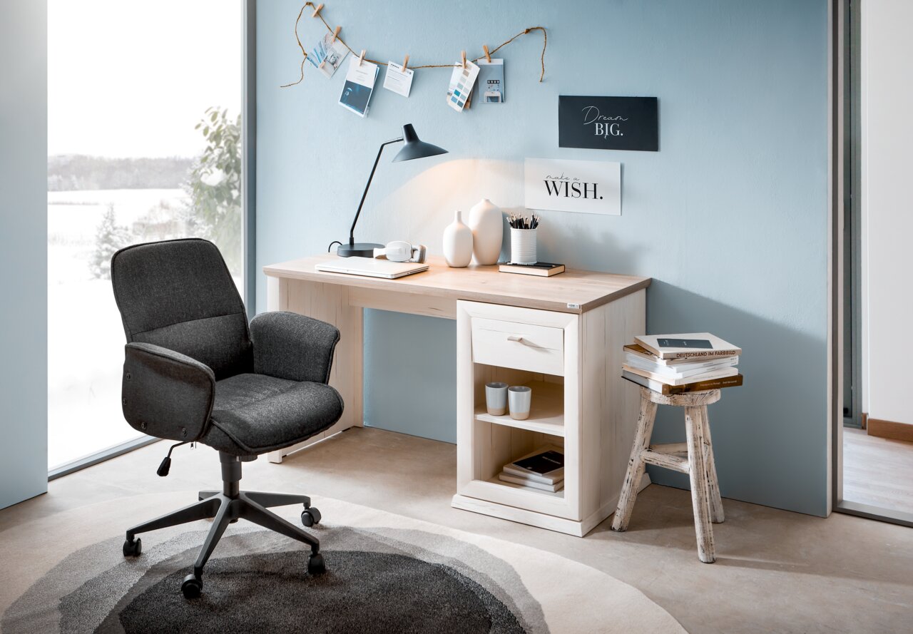 Moderner Schreibtisch in heller Holzoptik mit Schublade und Regal, seitliche Perspektive, dekoriert mit Lampe, Vasen und Büchern, neben einem großen Fenster mit Blick auf verschneite Landschaft.